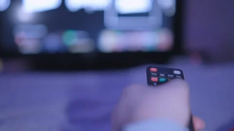 Sitting on sofa with remote, person enjoys watching TV with blurry screen in the Stock Footage 276435204