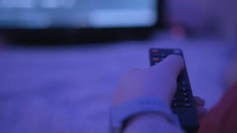 Sitting on sofa with remote, person enjoys watching TV with blurry screen in the Video stock 276498485