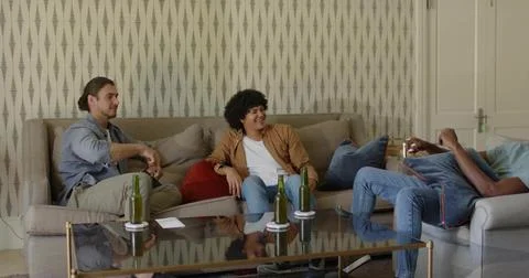 Sitting three men chatting on beige sectional in living room, with glass table Stock Photos