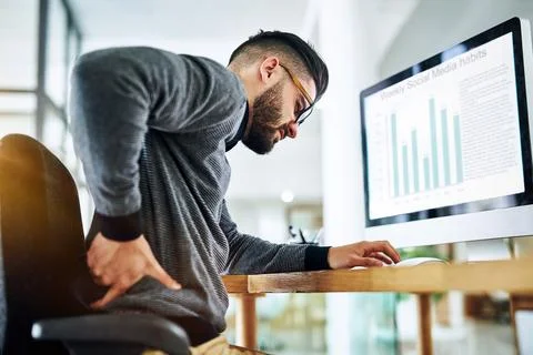 Sitting for too long can trigger unbearable back pain. a young designer Stock Photos