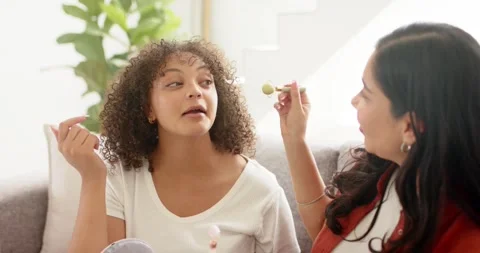 Sitting two friends wearing white V-neck and rust jacket on couch, applying Stock Footage 340964987