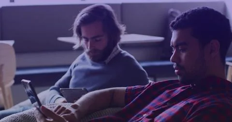 Sitting two men on couch in lounge, wearing red plaid, gray pullover, using Stock Photos
