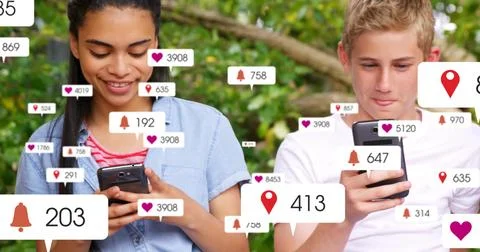 Sitting two teens using phones in park, showing notification bubbles and Stock Photos
