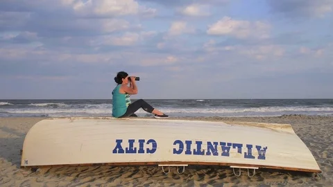 Sitting woman uses binoculars on beach at Atlantic City, New Jersey Stock Footage