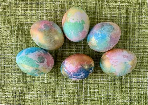 Six beautifully decorated Easter eggs in pastel colors rest on a textured green Stock Photos
