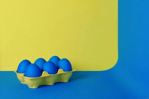 Six blue painted Easter eggs in yellow wrapping on blue and yellow background. Stock Photos