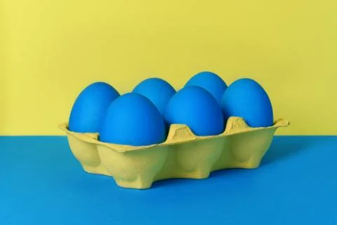 Six blue painted Easter eggs in yellow wrapping on blue and yellow background 스톡 사진