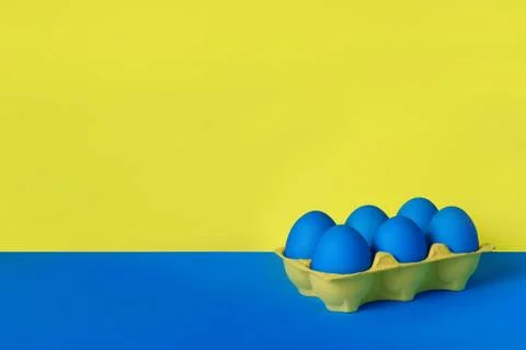 Six blue painted Easter eggs in yellow wrapping on blue and yellow background. Stock Photos