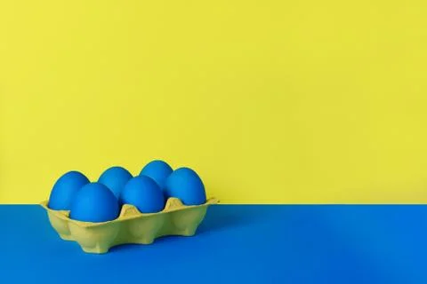 Six blue painted Easter eggs in yellow wrapping on blue and yellow background. Stock Photos