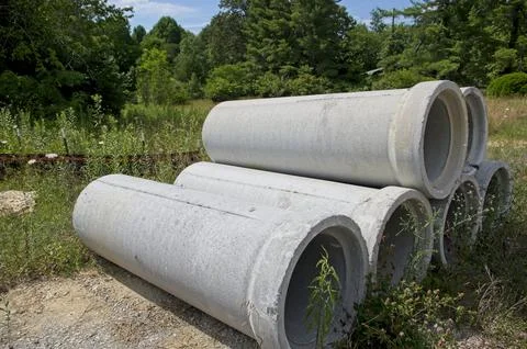 Six concrete drain pipe sections stacked in a grassy area Stock Photos