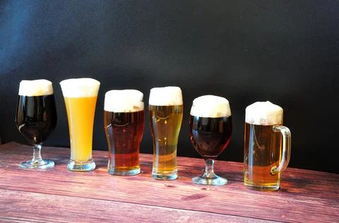 Six different glasses with different types of beer are in a row on a wooden t Stock Photos