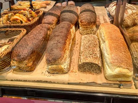 Six diverse freshly baked bread loaves displayed on a wooden board in a rus.. Stock Photos