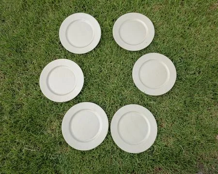 Six empty beige wicker textured plates arranged in a circle on green grass .. Fotos de archivo
