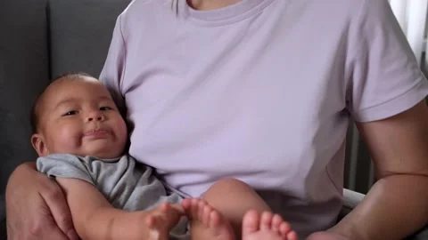 A six-month-old baby looks into the camera, holding his leg, touches his toes Stock Footage 201289341