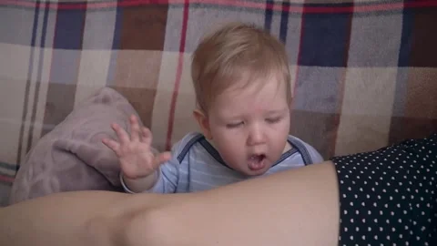 A six-month-old boy sits on the couch at home, yawns and then bites his mother's Stock Footage 308252418