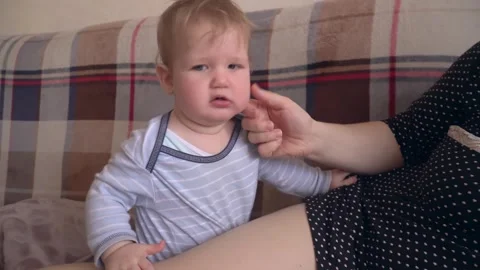 A six-month-old boy sits on the couch at home, yawns and then bites his mother's Stock Footage 320795029