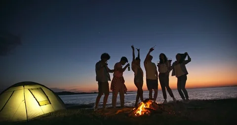 Six old multiethnic friends dncing on the beach near bonfire with drinks in Stock-Footage 94721590