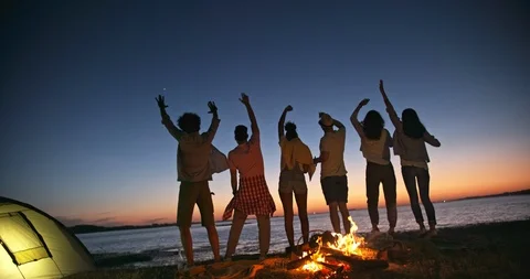 Six old multiethnic friends dncing on the beach near bonfire with drinks in Stock Footage 96445843
