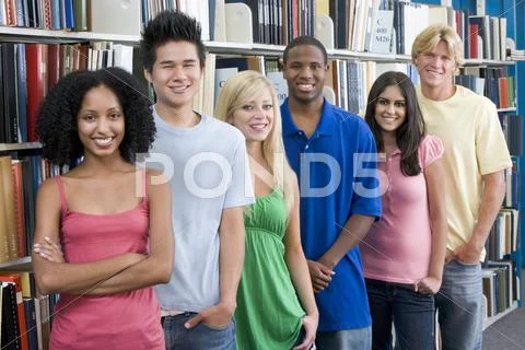 Six people in library standing by bookshelves Stock Photos