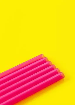 Six pink plastic drinking straws on yellow board, forming diagonal line - Foto stock