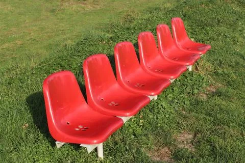 Six plastic red sets with blue are located in a row on green grass. Seats for Stock Photos