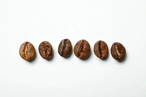 Six roasted coffee beans arranged neatly in a row against a plain white bac.. Stock Photos