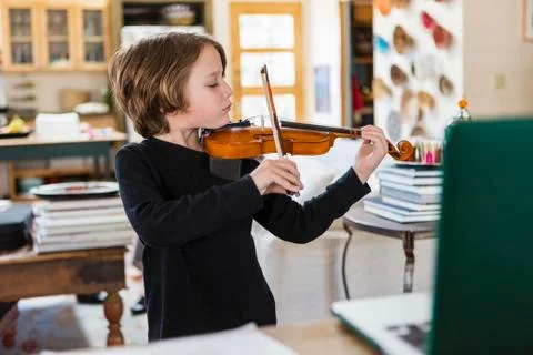 Six year old boy playing violin, having a remote video lesson in lockdown at Stock Photos