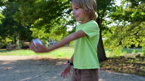 A six-year-old boy plays petanque in a sunny park, throwing a metal ball. He Video stock 284036648