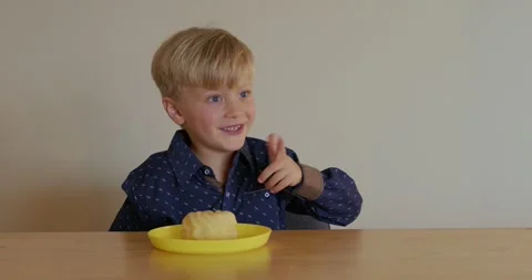 A six-year-old boy sitting at the table in a blue shirt wants to eat a donut and Video stock 320648349