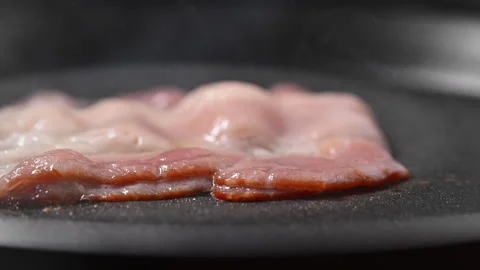 Sizzling bacon with flames, spattering fat, and rising smoke. 動画素材 317451930