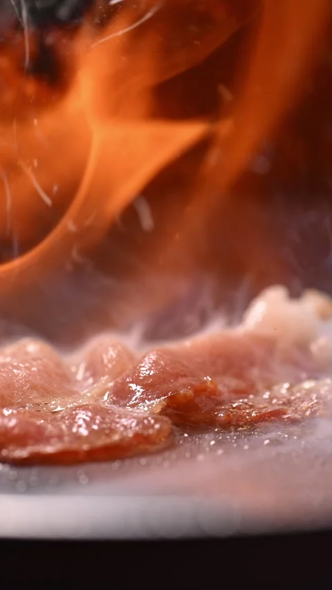 Sizzling bacon with flames, spattering fat, and rising smoke. 動画素材 317452396