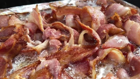 Sizzling brown Bacon strips. slices of bacon cooking on aluminum foil. 스톡 동영상 334642220