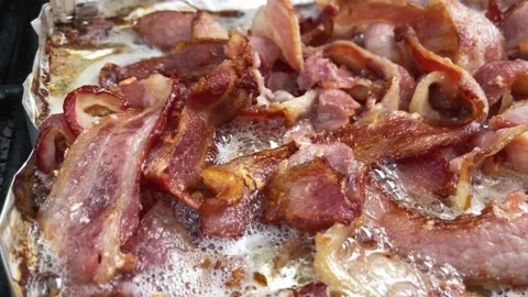 Sizzling brown Bacon strips. slices of bacon cooking on aluminum foil. 스톡 동영상 334642268