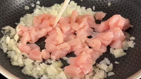 Sizzling chicken breast cubes with chopped onions in a frying pan for cooking Stock Footage 325072012