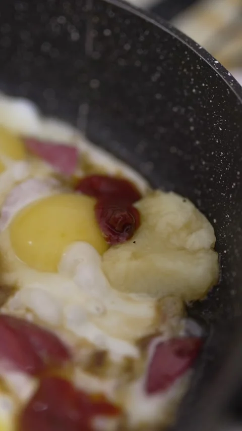 Sizzling fried eggs and sausage slices browning in a pan Stock Footage 333651468