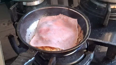 Sizzling ham slice frying in a hot metal skillet video footage Stock Footage 338134639
