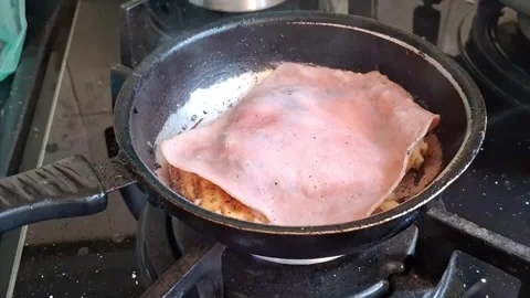 Sizzling ham slice frying in small kitchen skillet video footage Stock Footage 338134635