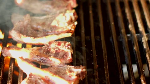 Sizzling lamb chops over flames on outdoor barbecue being flipped using tongs Stock-Footage 332120670