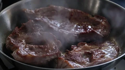 Sizzling meat steaks frying in a pan with bubbling hot oiil Stock Footage 336097335
