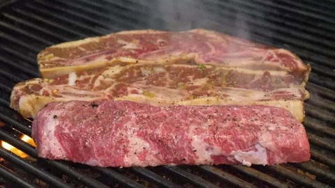 Sizzling Raw Beef Steaks on a Hot Grill with Rising Smoke, Close-Up 스톡 동영상 332815300