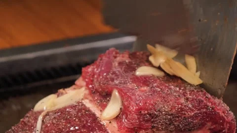 Sizzling Wagyu Beef Steak with Fresh Garlic Slices on a Tabletop Grill Stock Footage 333600166