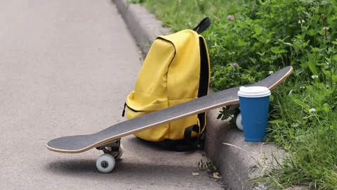 Skateboard, yellow backpack and coffee on the side of the road Vídeos de archivo 335618646