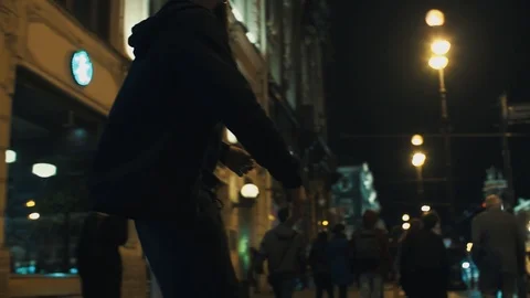 Skateboarder man in black hoodie rides on crowded night city sidewalk Stock Footage
