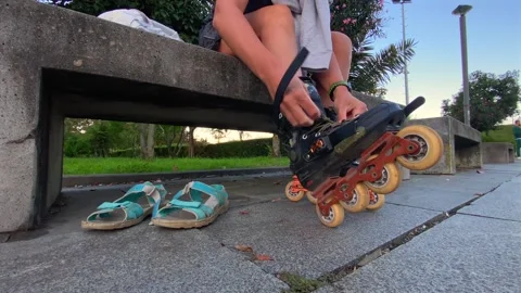 Skater fastening inline skate strap, low-angle close-up beside a park bench Stock Footage 345361726
