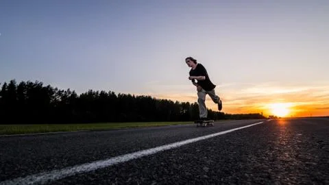 Skater make pushing on empty road at the beautiful sunset Stock Photos