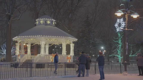 Skaters move past small town gazebo at night lit up for Christmas 動画素材 249613786