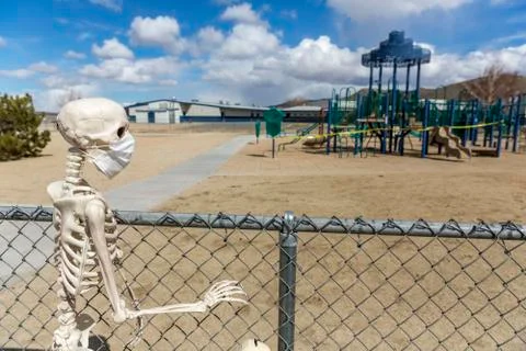 Skeleton behind fence looking at an empty closed park on a nice day Foto stock