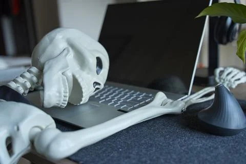 Skeleton collapsed with head resting on laptop keyboard at office desk Stock Photos