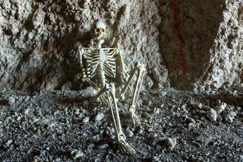 Skeleton in a dark cave in the ground lying on rocks Stock Photos