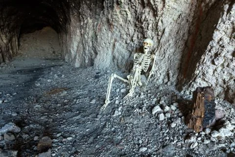 Skeleton in a dark cave in the ground lying on rocks Stock Photos